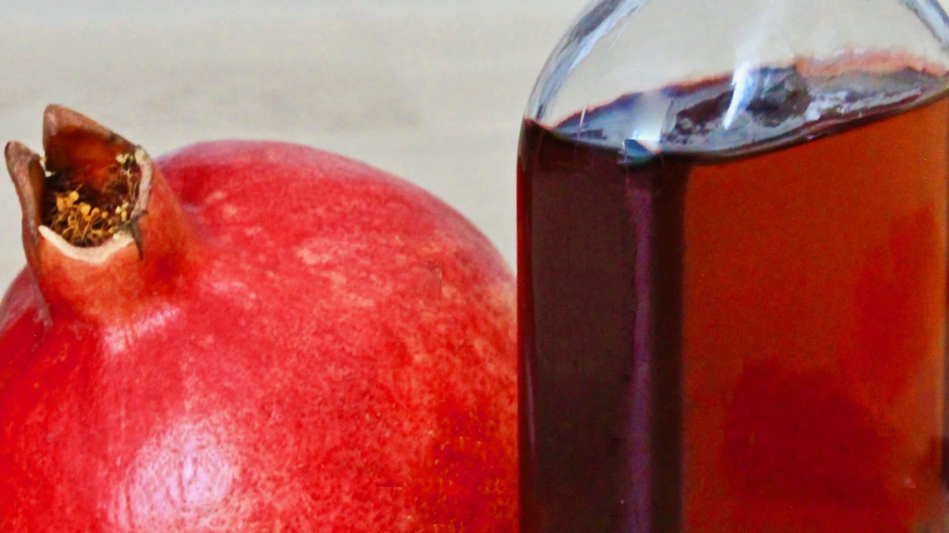 Une grenade posée à côté d'une bouteille de sirop de grenadine maison
