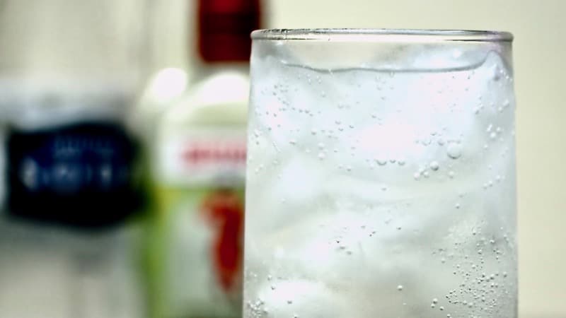Gros plan sur un Tom Collins cocktail avec une bouteille de Gin Beefeater en fond
